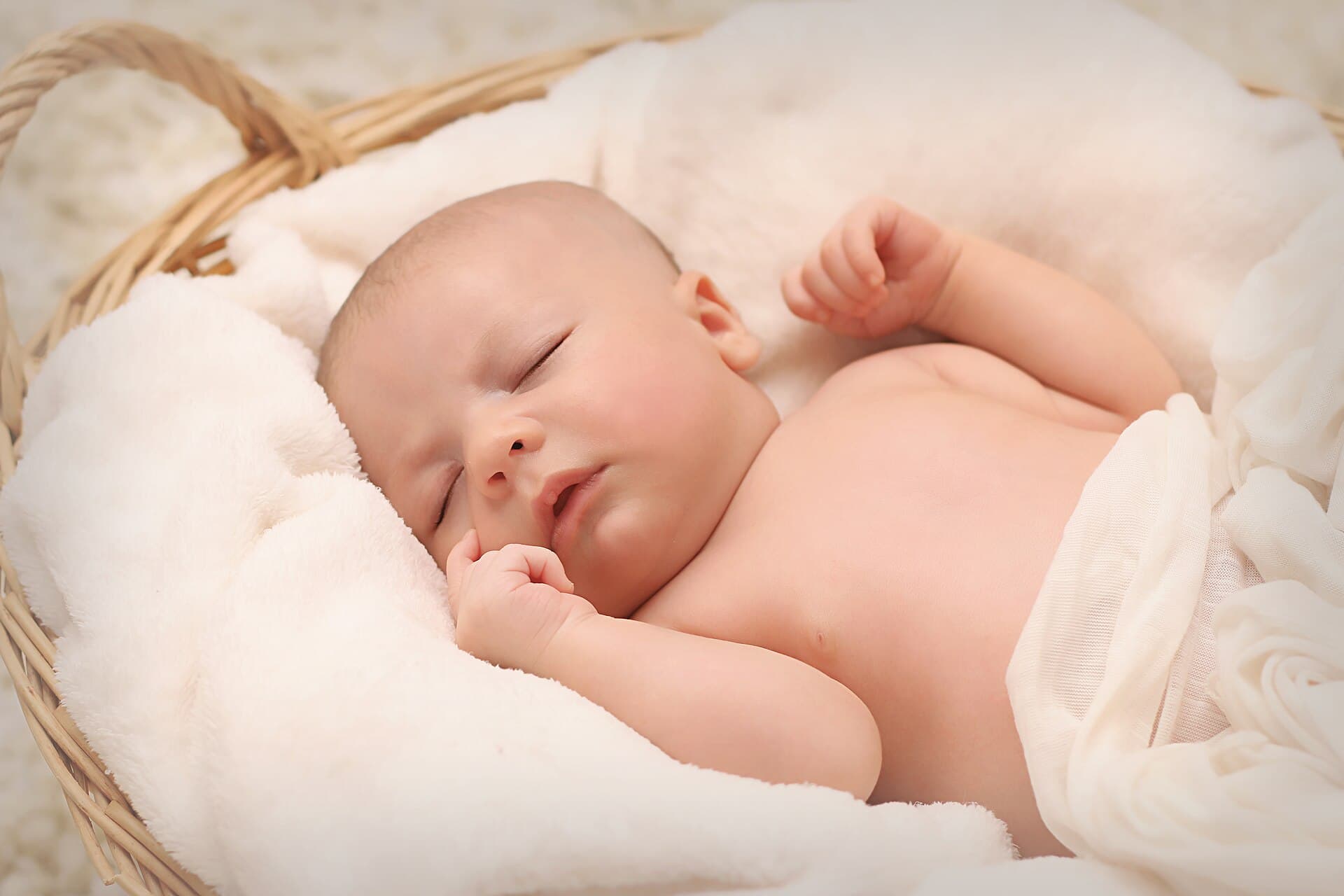 Pasgeboren baby slaapt in een rieten mand op een witte vacht