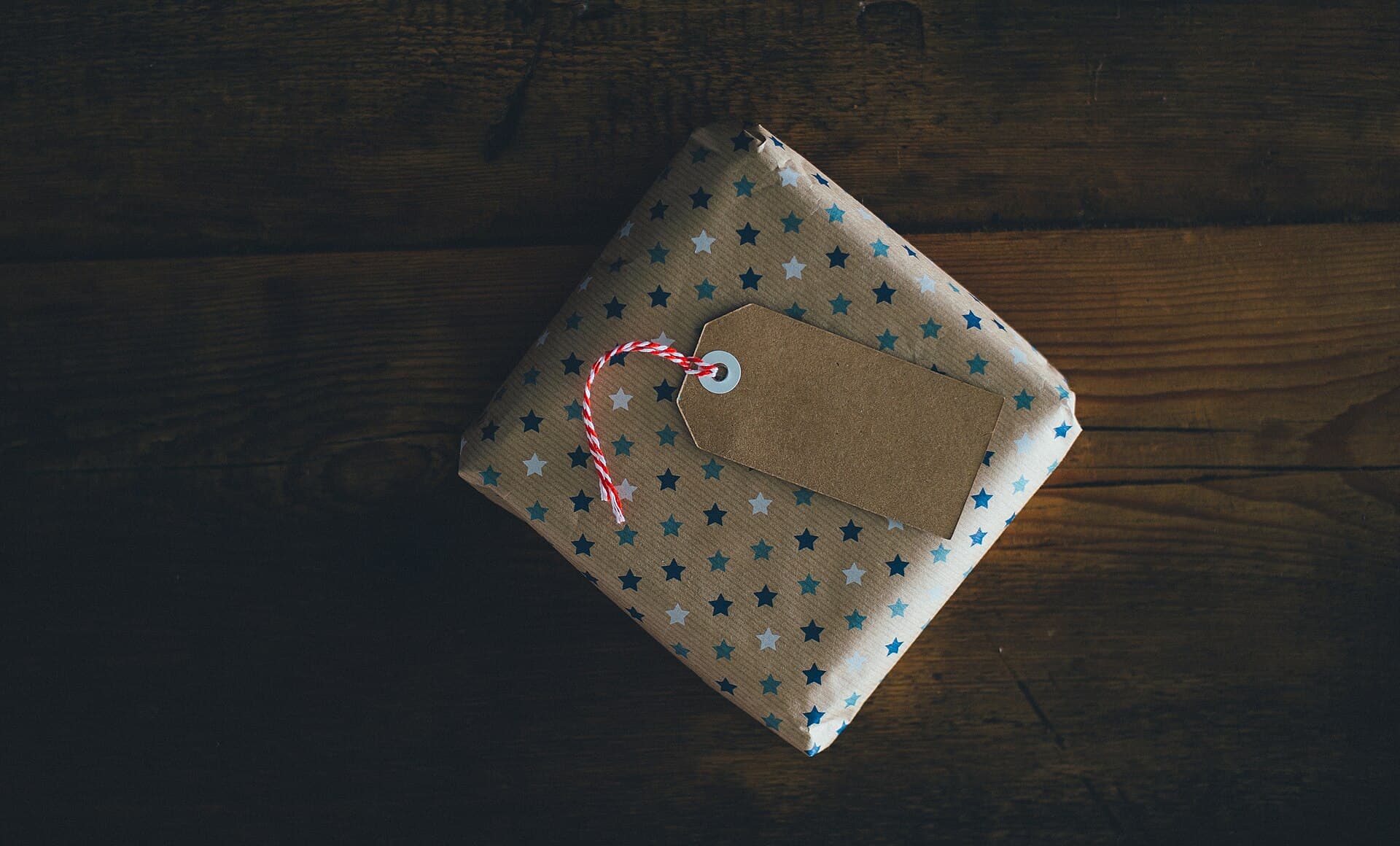 Een klein cadeau in papier met sterretjes, met een kartonnen label en een rood-wit touwtje, op een houten tafel
