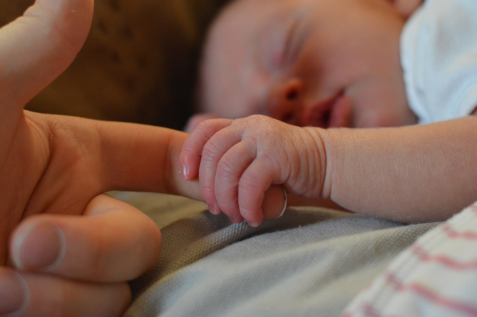 Een babyhandje houdt een vinger vast, op een bed in zacht licht