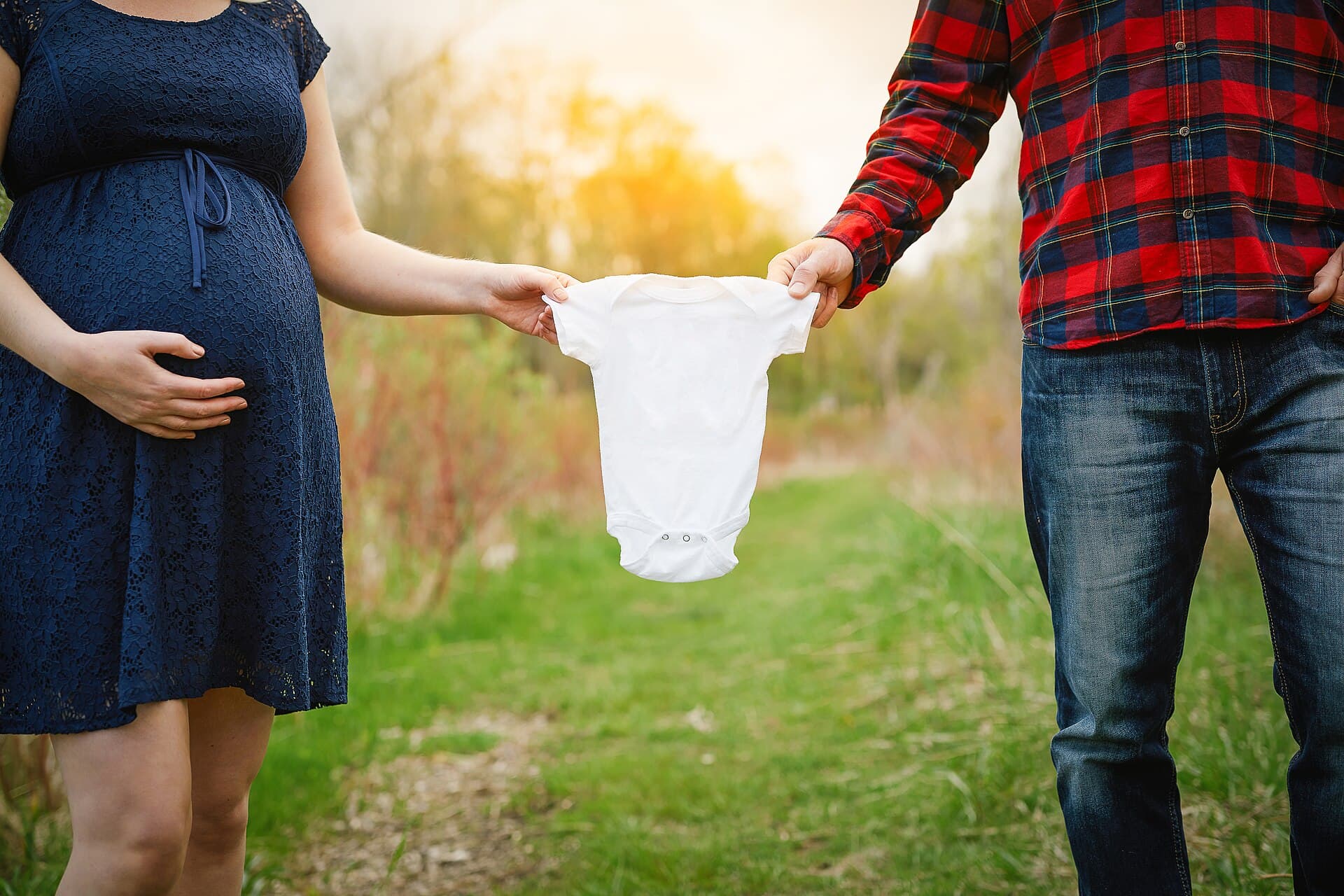 Een stel houdt een wit babyrompertje tussen zich in, buiten in tegenlicht