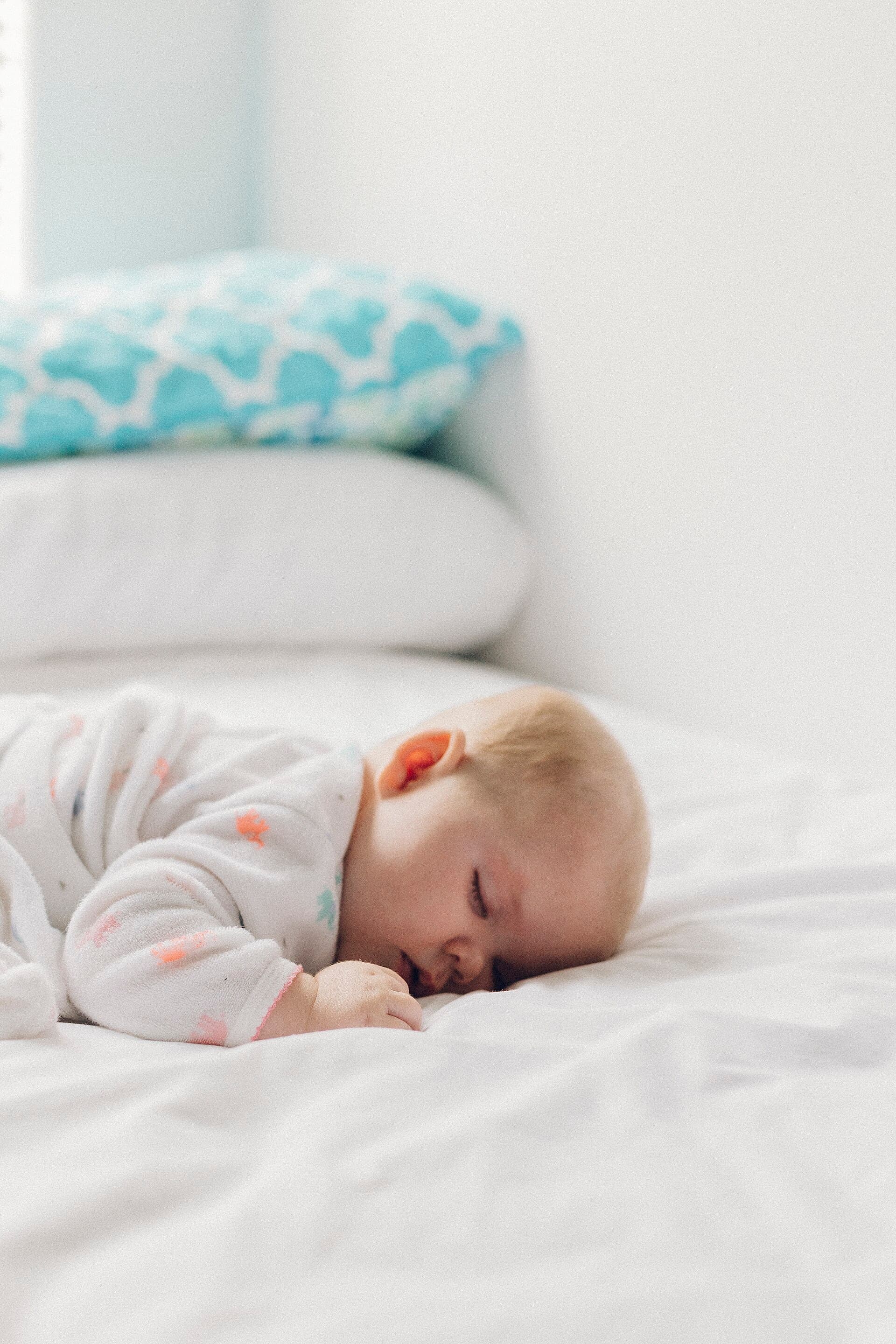 Een slapende baby op een wit laken, met een kleine hand naast het hoofd