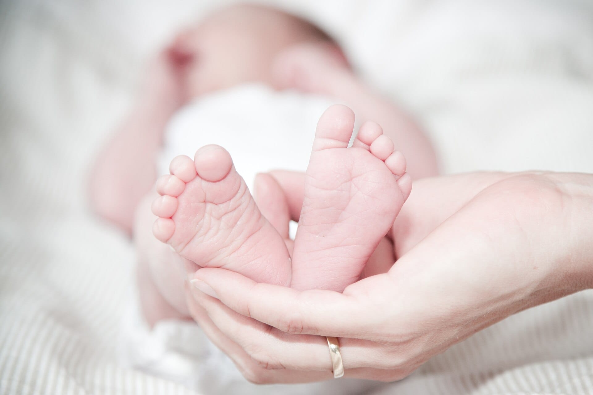 Een ouder houdt de voetjes van een pasgeboren baby vast, op zacht, licht beddengoed